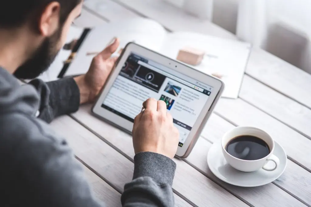 Persona che naviga su un tablet accanto a una tazza di caffè