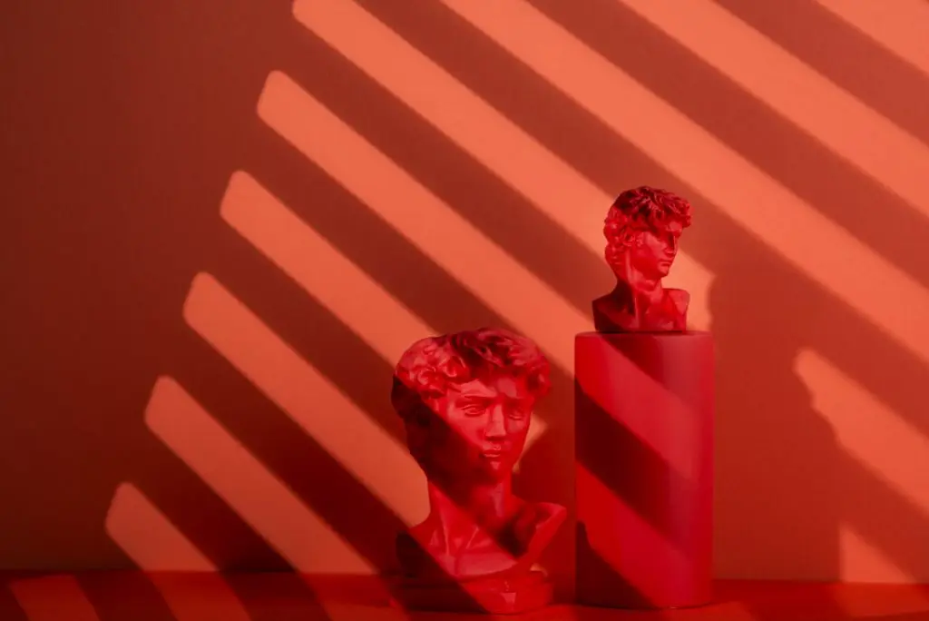 Busti in gesso su fondo corallo con ombre a righe