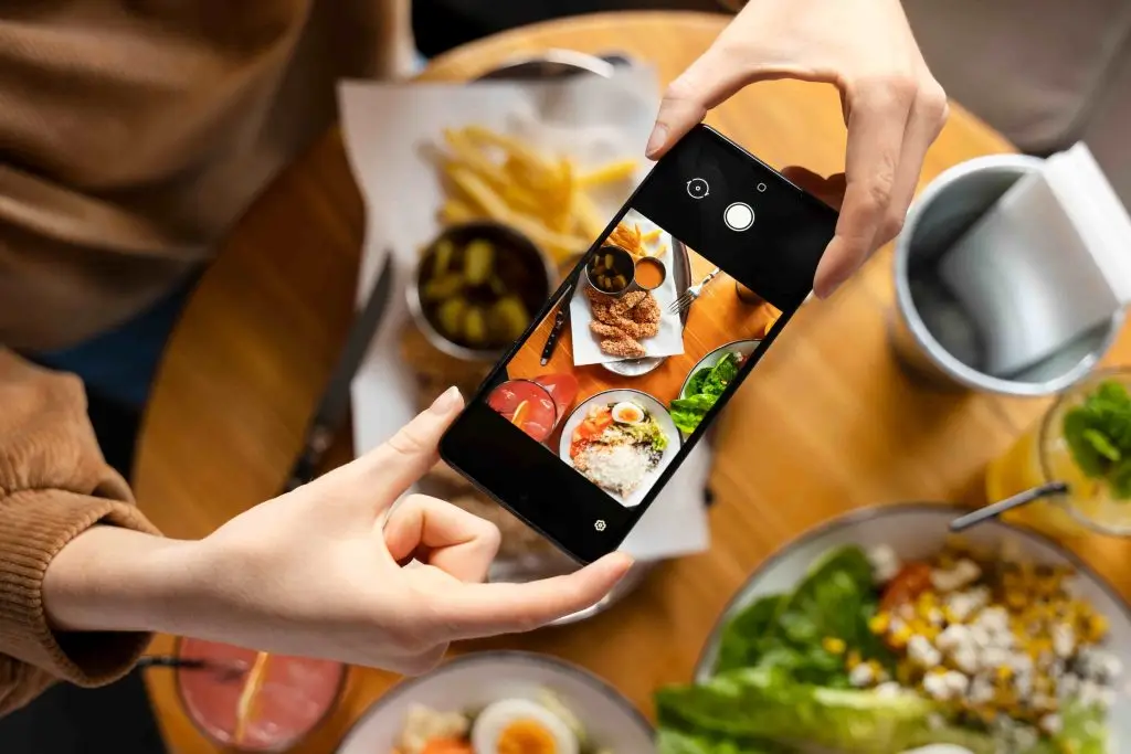 Cliente che fotografa con lo smartphone i piatti del pranzo al ristorante